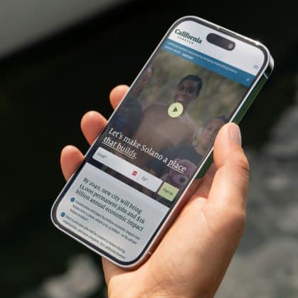 Hand holding smartphone displaying California Forever website with community imagery and email signup form